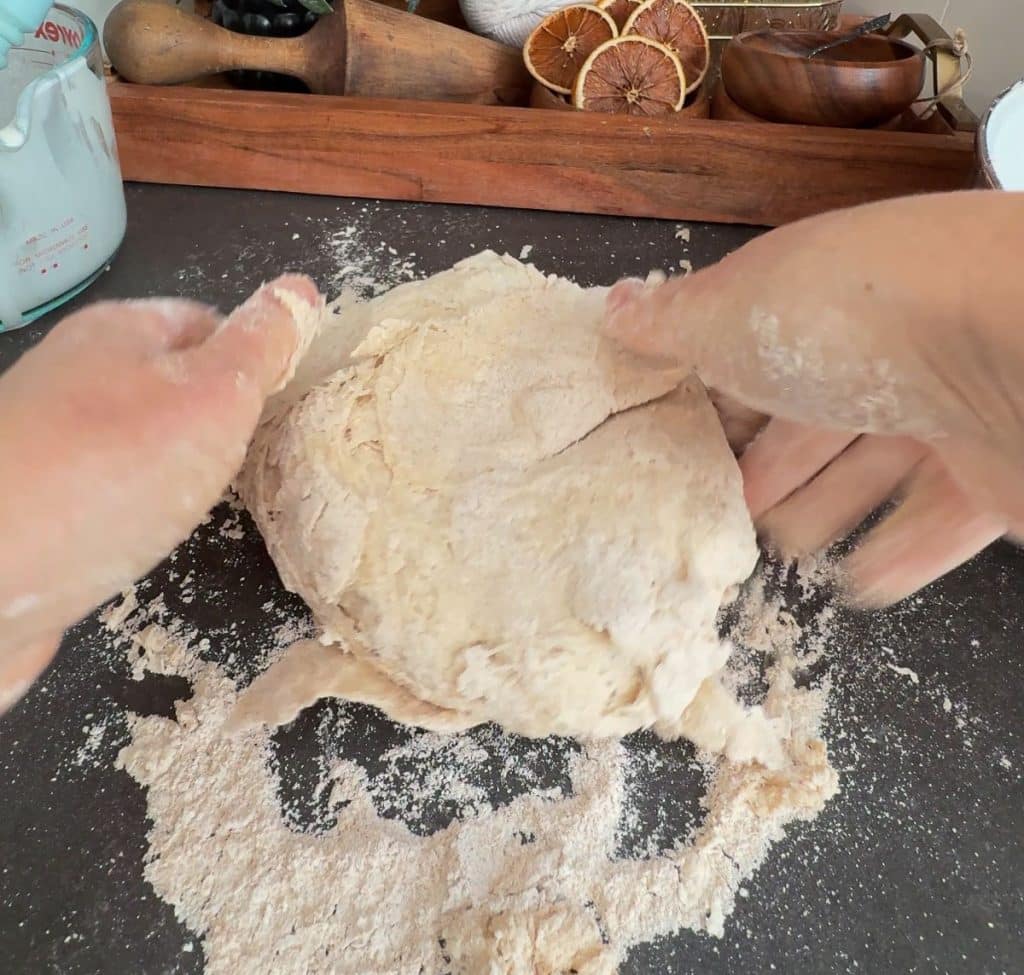 kneading soda bread dough on a black countertop with kitchen decor in the background