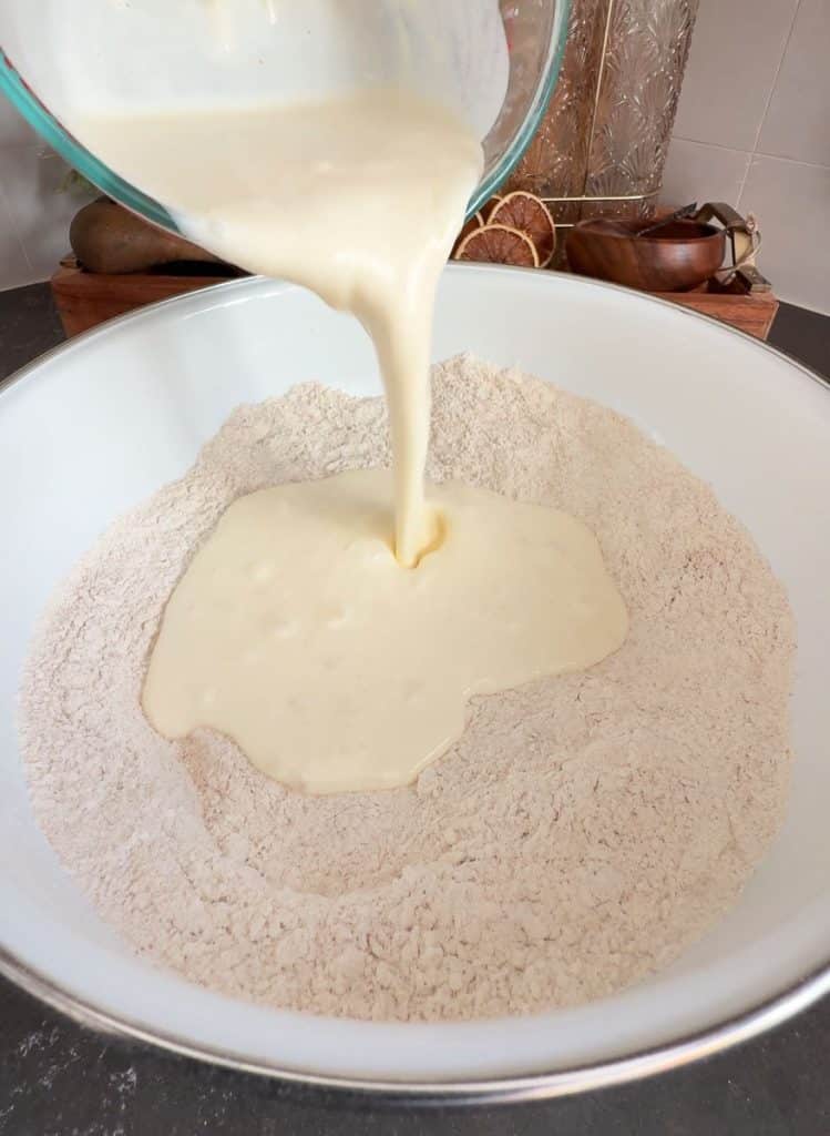 adding buttermilk mixture to flour. pouring from a glass measuring cup into a white mixing bowl