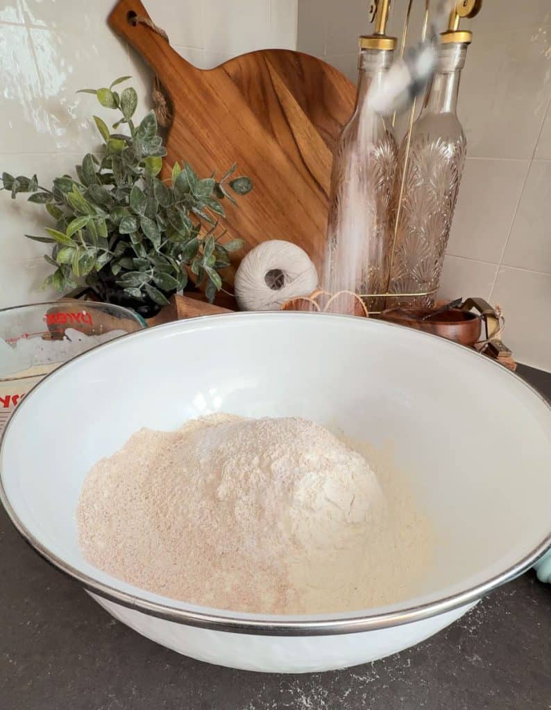 measuring flour into a bowl and adding kosher salt. white bowl on a black countertop with kitchen decor in the background