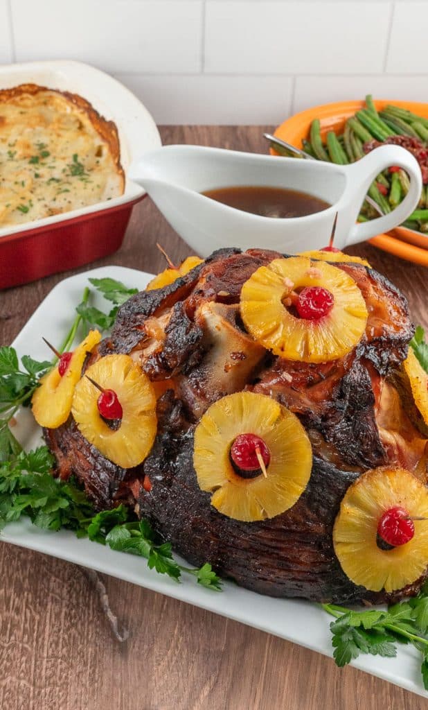 photo of ham with pineapple slices, scallop potatoes and green beans with a dish of gravy in the background