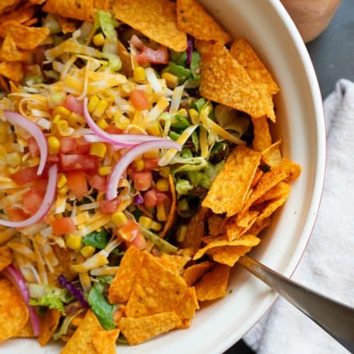 large bowl of taco salad on a black counter top with a jar of salad dressing in the upper right hand corner of the photo