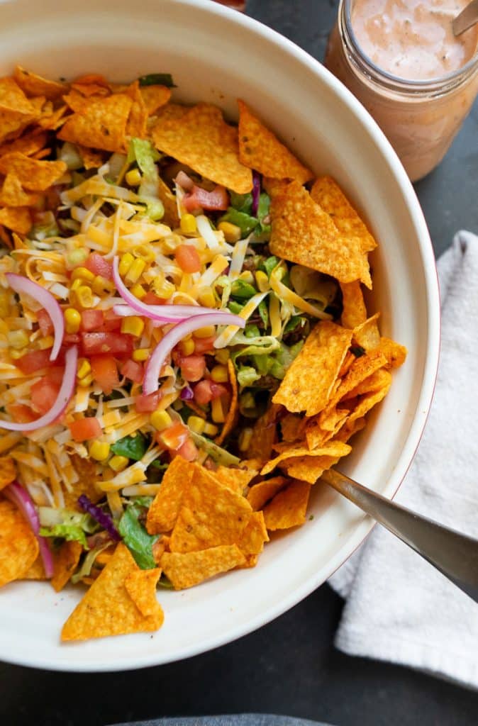 large bowl of taco salad on a black counter top with a jar of salad dressing in the upper right hand corner of the photo