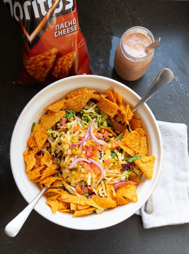 photo of a large bowl with dorito taco salad in it with a jar of salad dressing in the upper right hand corner and a bag of doritos in the upper left hand corner