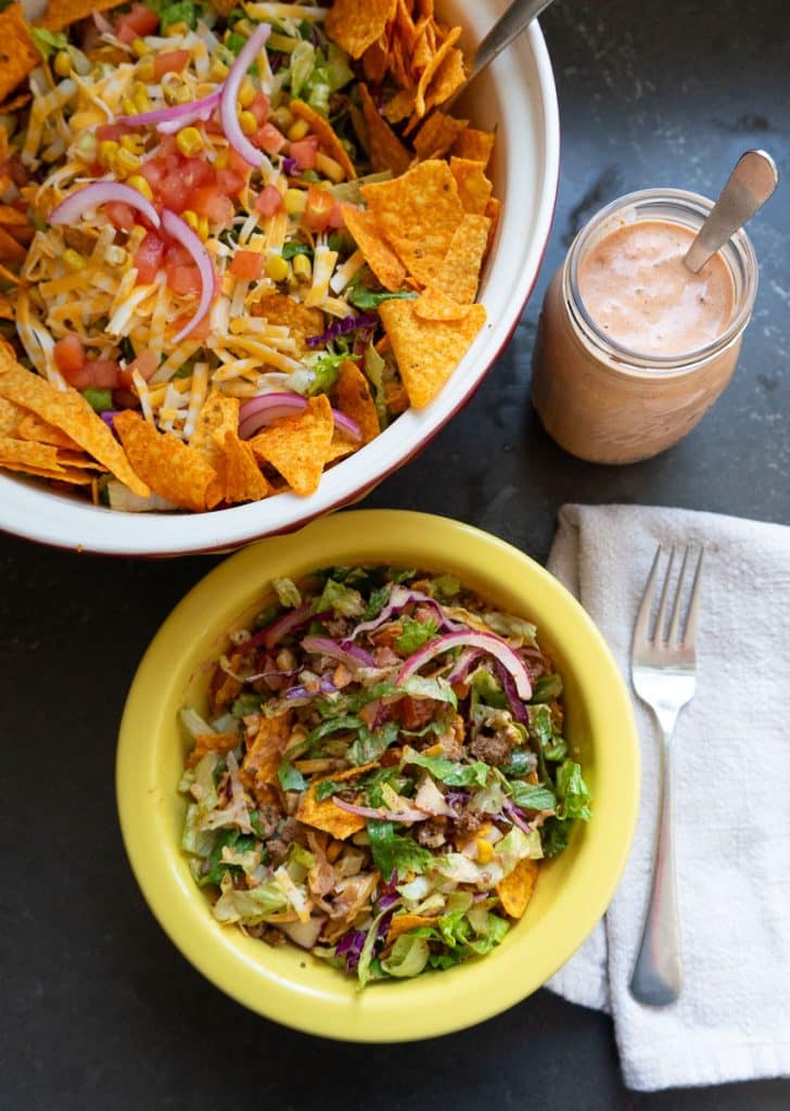 large bowl of taco salad with a individual portion sized bowl next to it with a jar of thousand island dressing