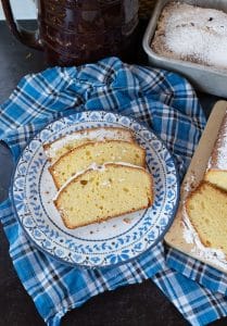 Slices of pound cake on a blue rimmed plate. next to the whole loaf of pound cake on a cutting board