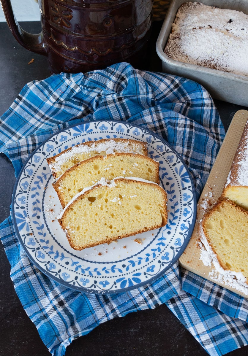 Slices of pound cake on a blue rimmed plate. next to the whole loaf of pound cake on a cutting board