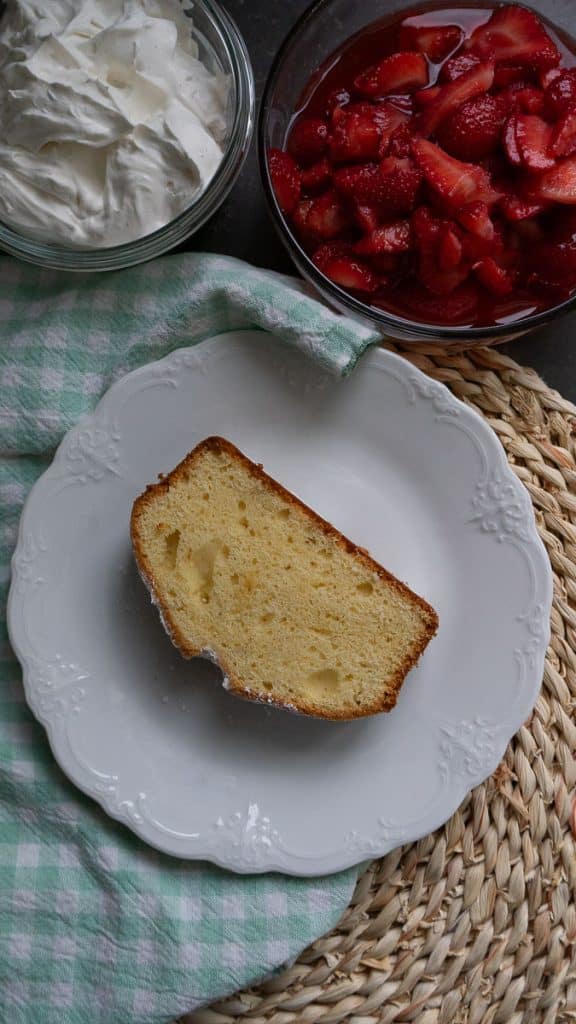 slice of pound cake on a plate with a bowl of whipped topping and a bowl of fresh cut strawberries in the top of the photo