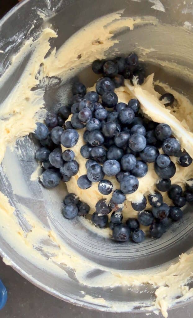 adding blueberries to the batter in blow, white spatula is folding them in