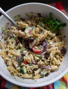 bowl of greek pasta salad with a silver spoon lifting a spoonful of pasta salad out of the bowl