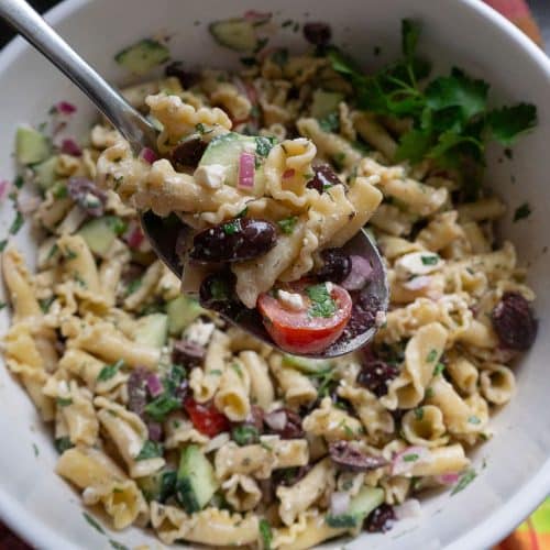 bowl of greek pasta salad with a silver spoon lifting a spoonful of pasta salad out of the bowl