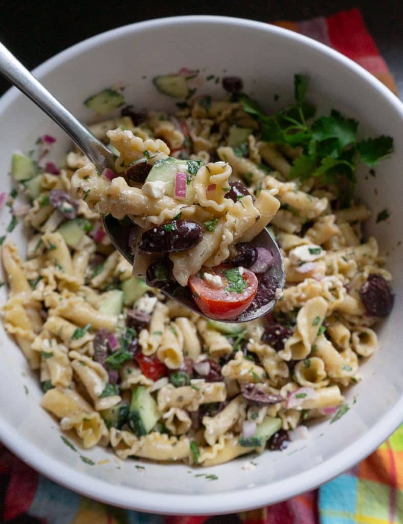 bowl of greek pasta salad with a silver spoon lifting a spoonful of pasta salad out of the bowl