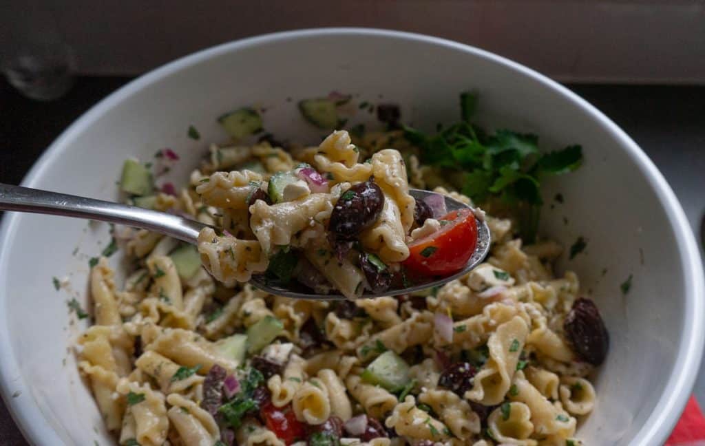 bowl of greek pasta salad with a silver spoon lifting a spoonful of pasta salad out of the bowl
