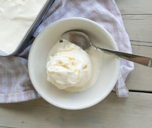 scoop of vanilla ice cream in a white bowl on a picnic table with a tan and white gingham cloth under the bowl