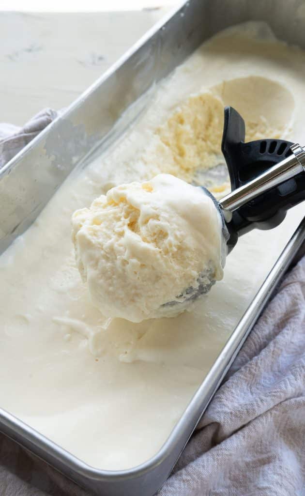 vanilla ice cream in a silver rectangle container with an ice cream scoop scooping out ice cream 