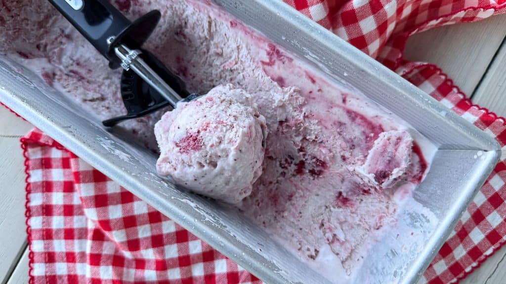 container of strawberry ice cream with an ice cream scoop full of ice cream laying in the container