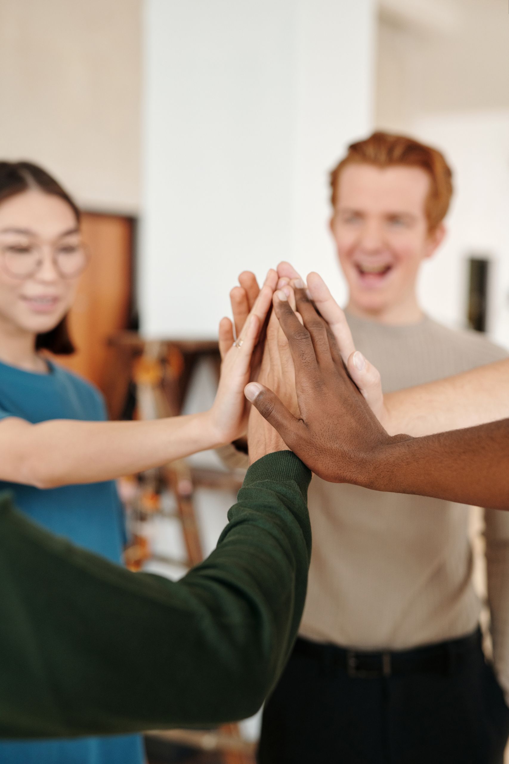 A diverse group of adults high-fiving to celebrate teamwork and unity indoors.
