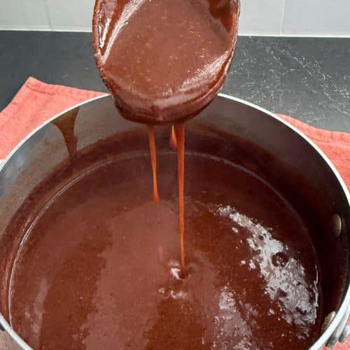 wooden spoon dripping enchilada sauce over saucepan full of enchilada sauce