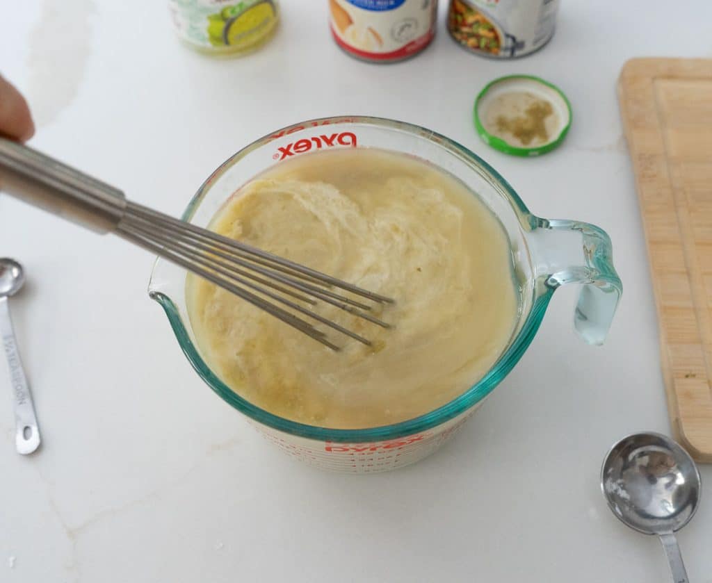 whisking ingredients together in a glass bowl on a white countertop 