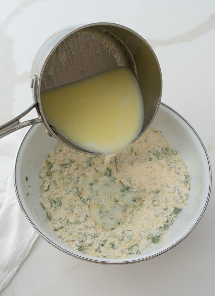 adding warm milk and butter to dry dumpling ingredients on a white kitchen countertop ingredients are in a white bowl