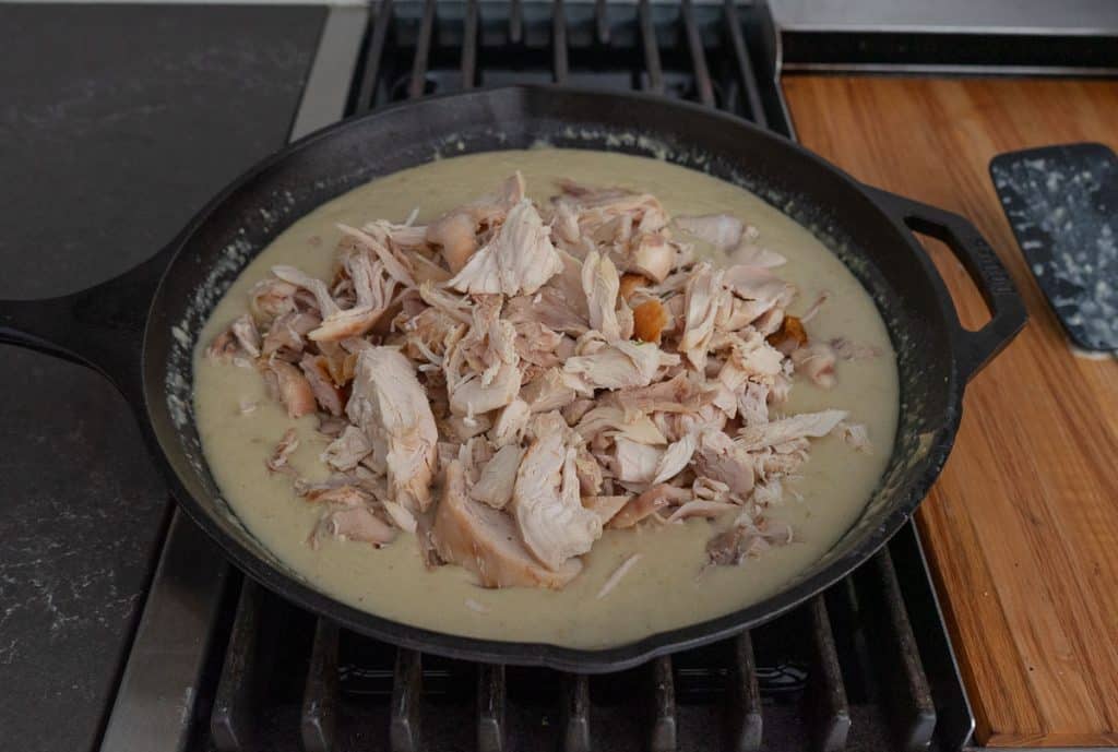 adding chicken to the gravy in a cast iron skillet on stovetop