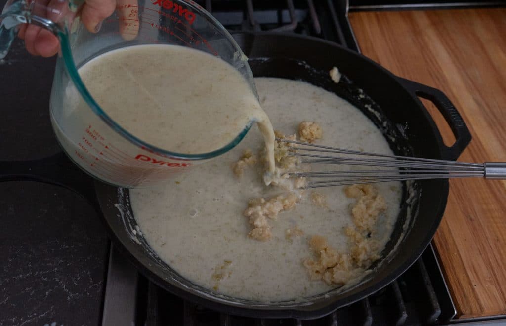 pouring liquid mixture into the skillet on stovetop, there is a whisk in the pan 