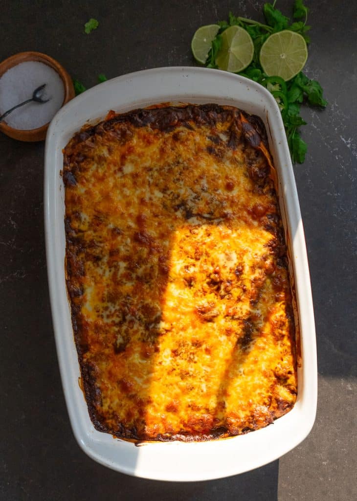 casserole dish of beef and bean enchiladas setting on black countertop with a dish of salt and some cut limes in the top of the photo