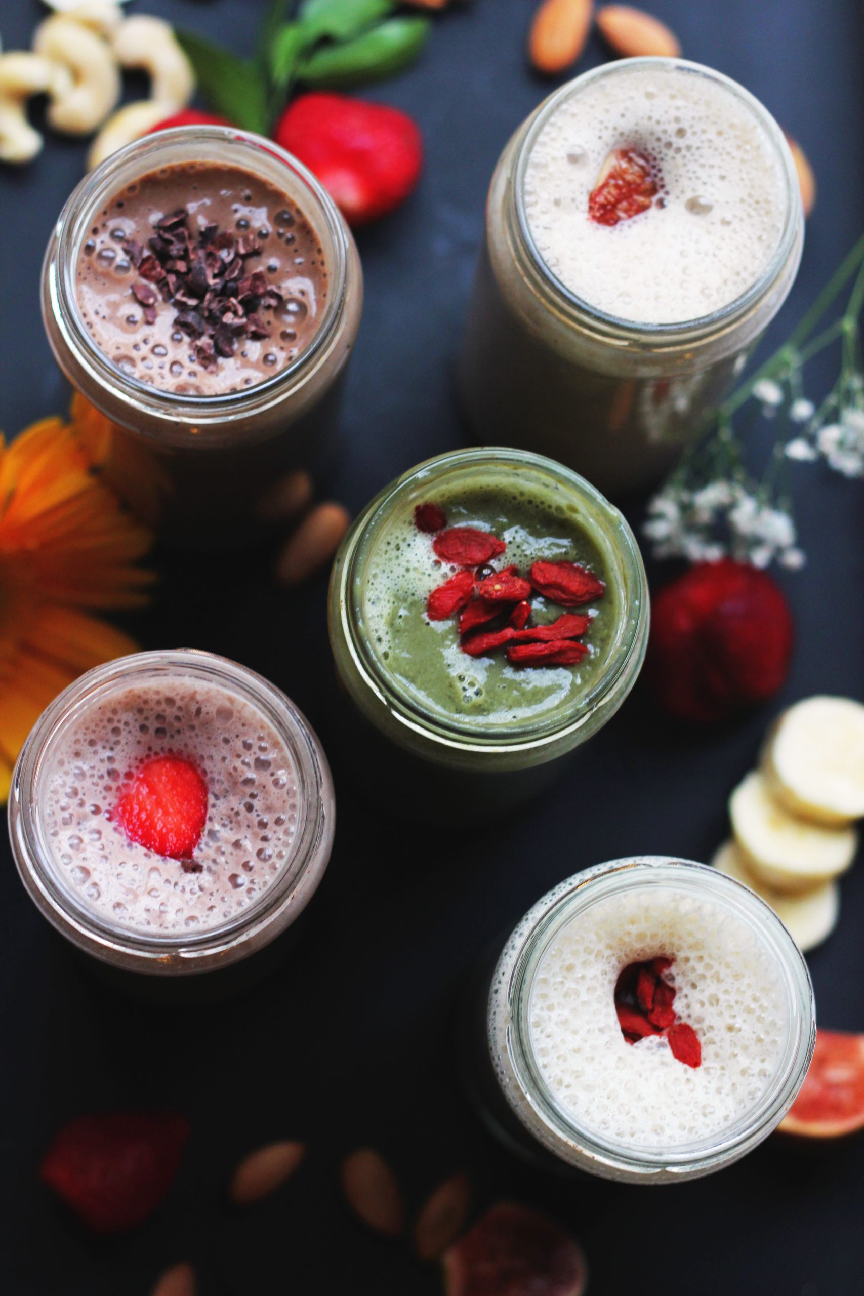 Colorful smoothies with toppings presented in jars on a dark background, highlighting natural ingredients.