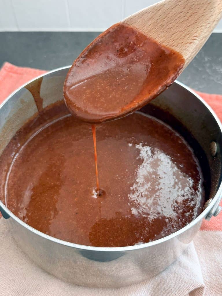 pan full of red enchilada sauce with a wood spoon over the pan with sauce dripping off the spoon