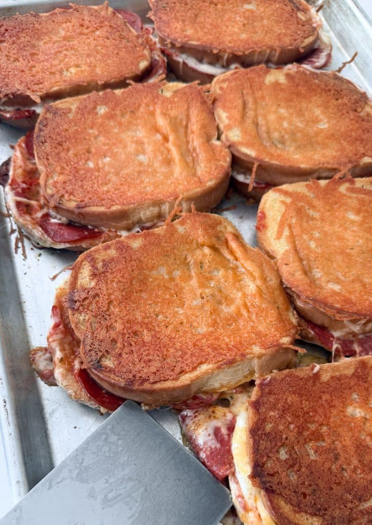 pan of whole uncut parmesan encrusted grilled cheese sandwiches, there is a metal spatula in the bottom left of the photo