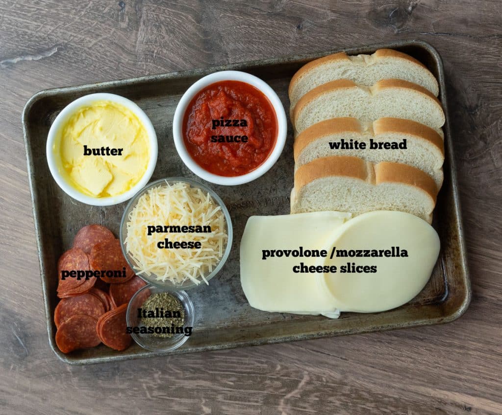 ingredients on a baking sheet clockwise starting at noon pizza sauce, white bread, mozzarella cheese slices, parmesan cheese, Italian seasoning, pepperoni, butter,