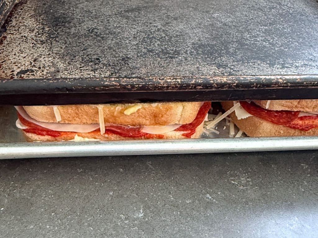 side view of the parm crusted pepperoni pizza grilled cheese sandwiches between the two baking sheets