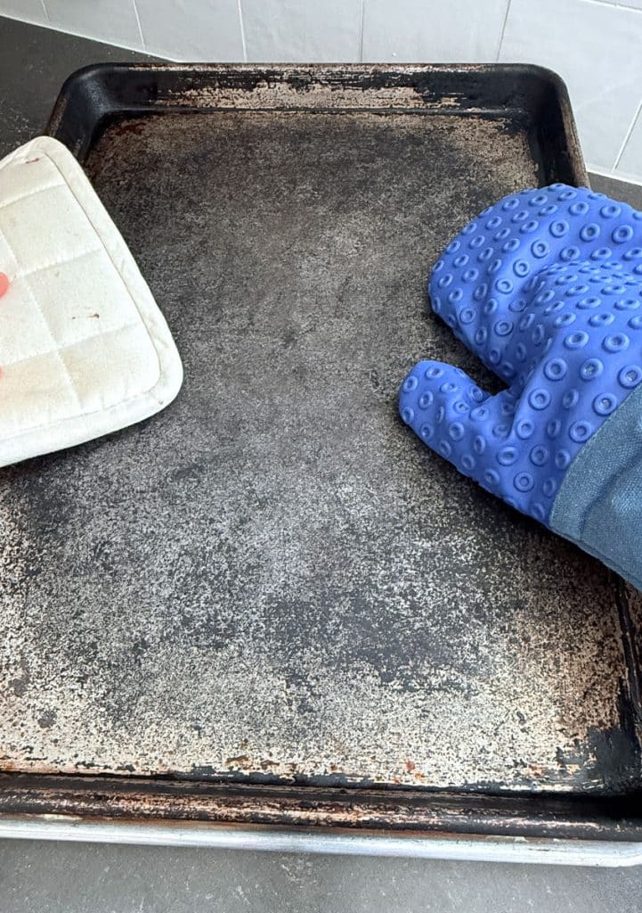 Placing hot baking sheet on top of grilled cheese sandwiches two hands with oven mitts are pressing down on the hot pan