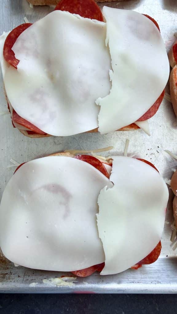 bread on a baking sheet with pizza sauce and a piece of provolone on top