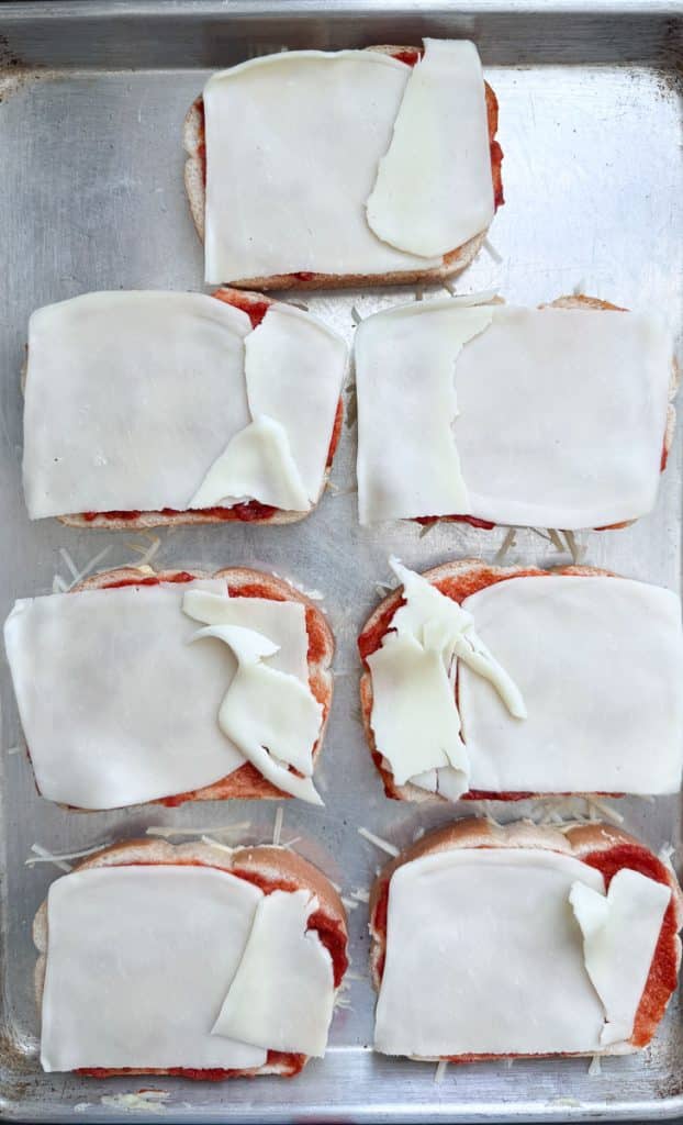 bread on a baking sheet with pizza sauce and a piece of provolone on top