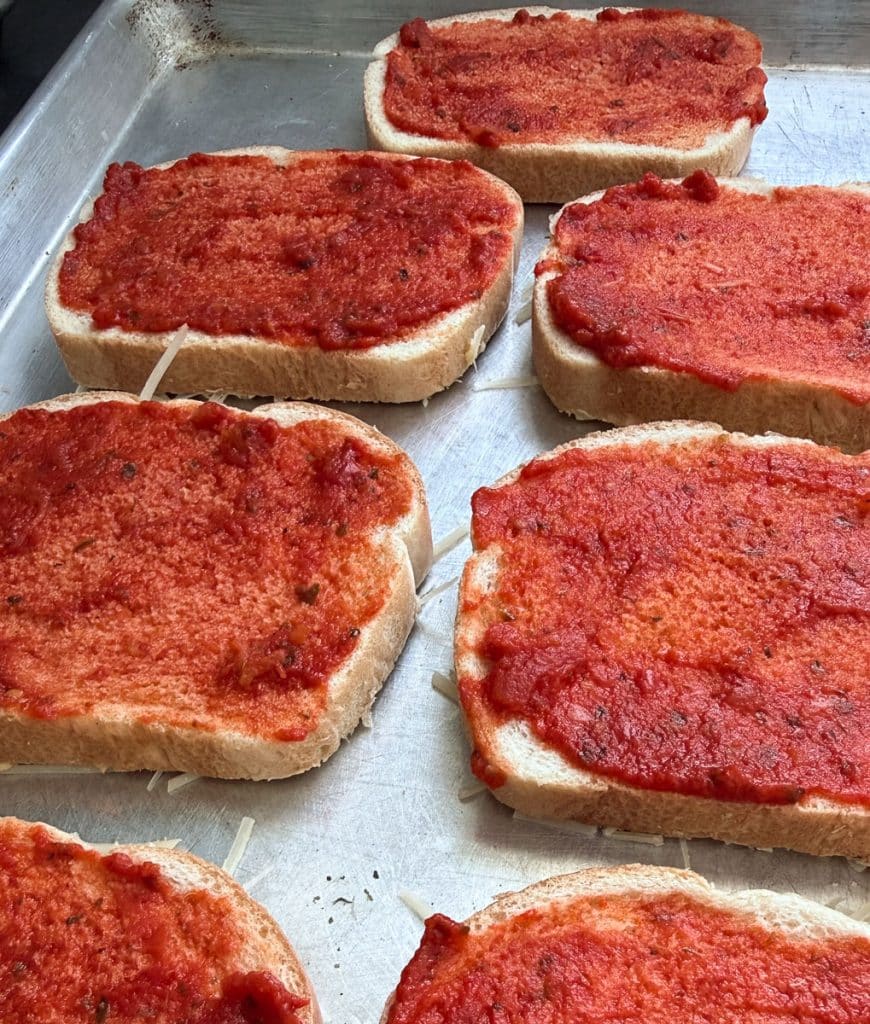 bread on a baking sheet spread with a layer of pizza sauce