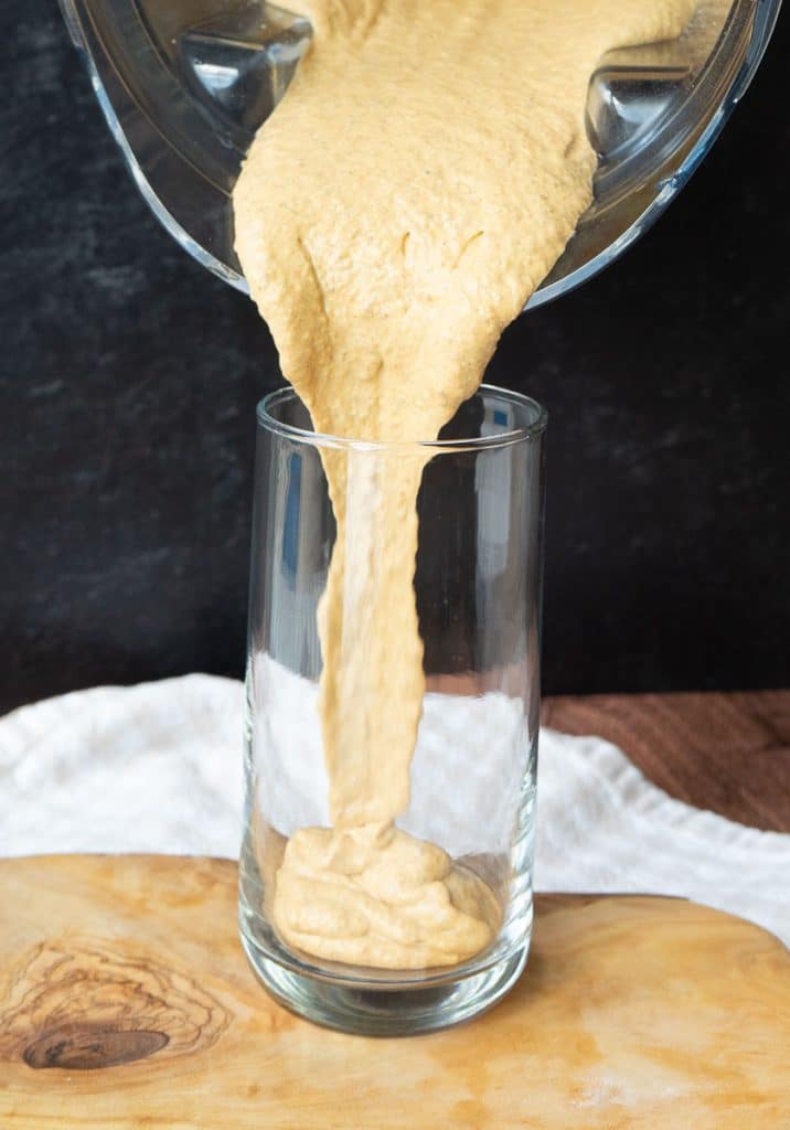 pouring pumpkin spice protein shake into a glass on a wood board the background is black