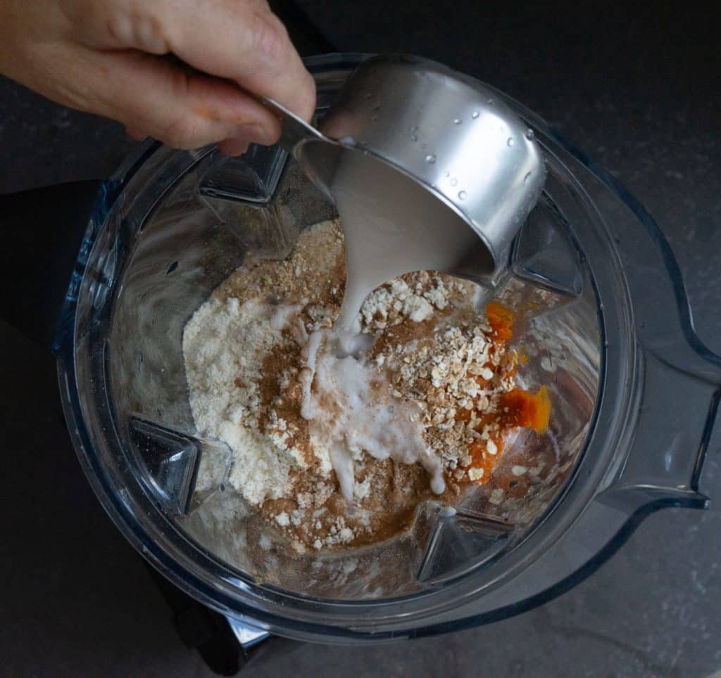 adding all the ingredients into a blender, pouring the almond milk into the top of the blender