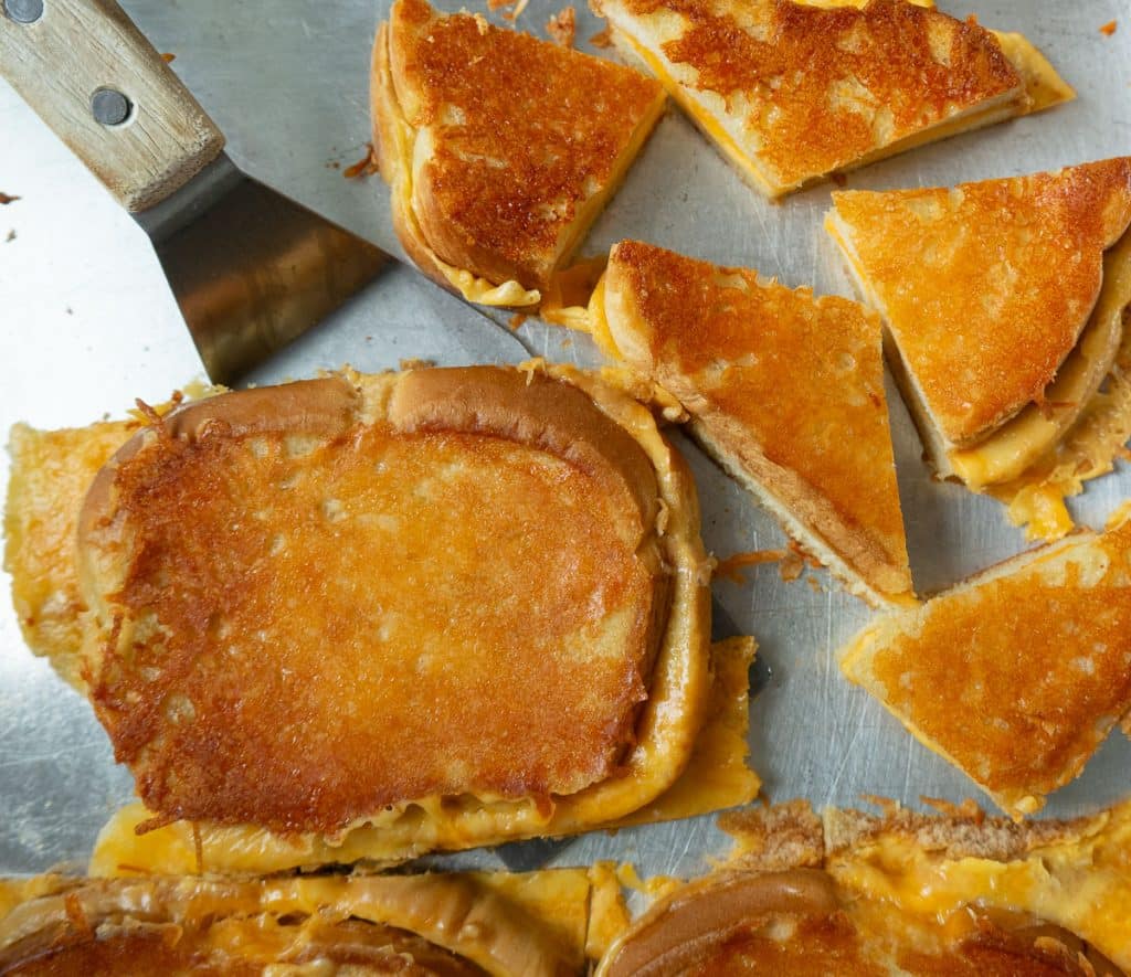 grilled cheese sandwiches on a sheet pan one as a metal spatula underneath it, some are cut into quarters