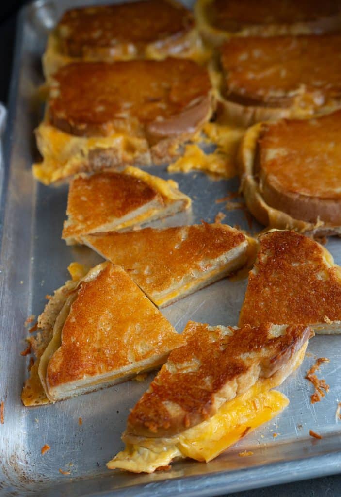 sheet pan of grilled cheese sandwiches some are whole and some are cut into quarters