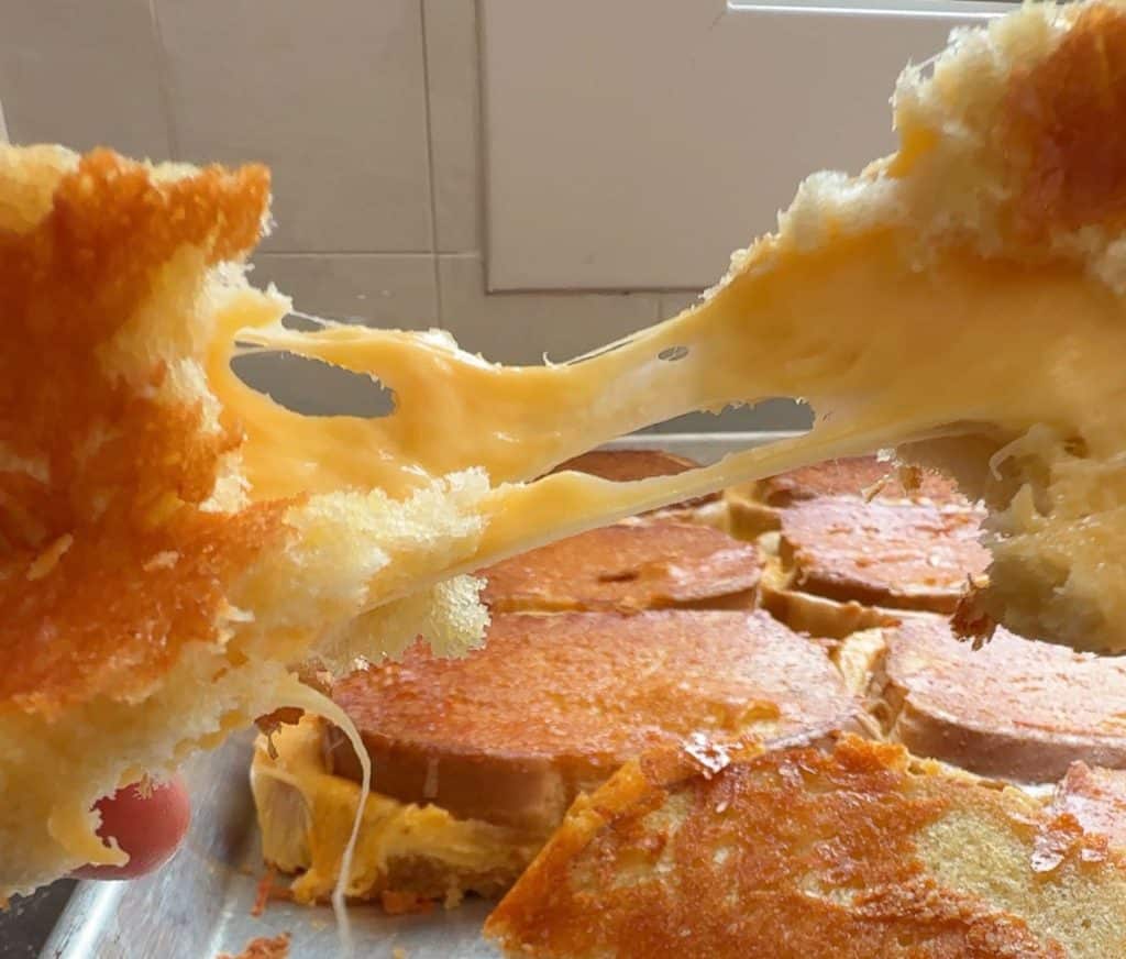 cheese pull of grilled cheese sandwich over a whole sheet pan of grilled cheese sandwiches
