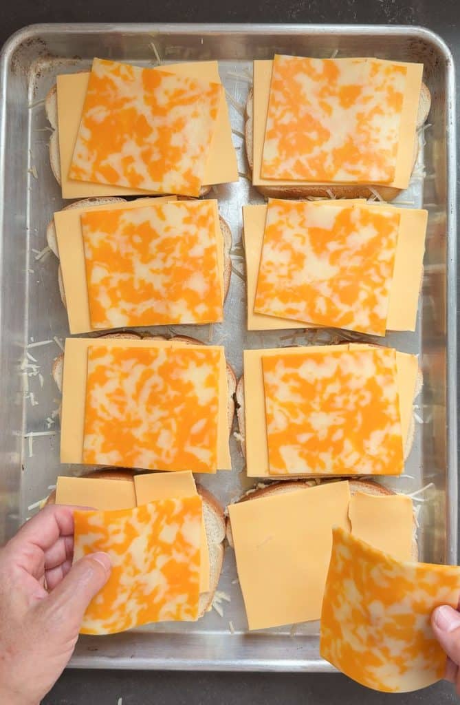 laying slices of american and colby jack cheese on top of bread slices on a baking sheet
