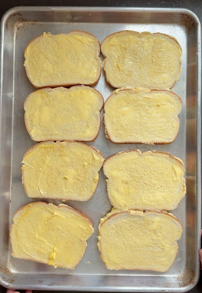 eight slices of white bread buttered and laid out in a single layer on a sheet pan